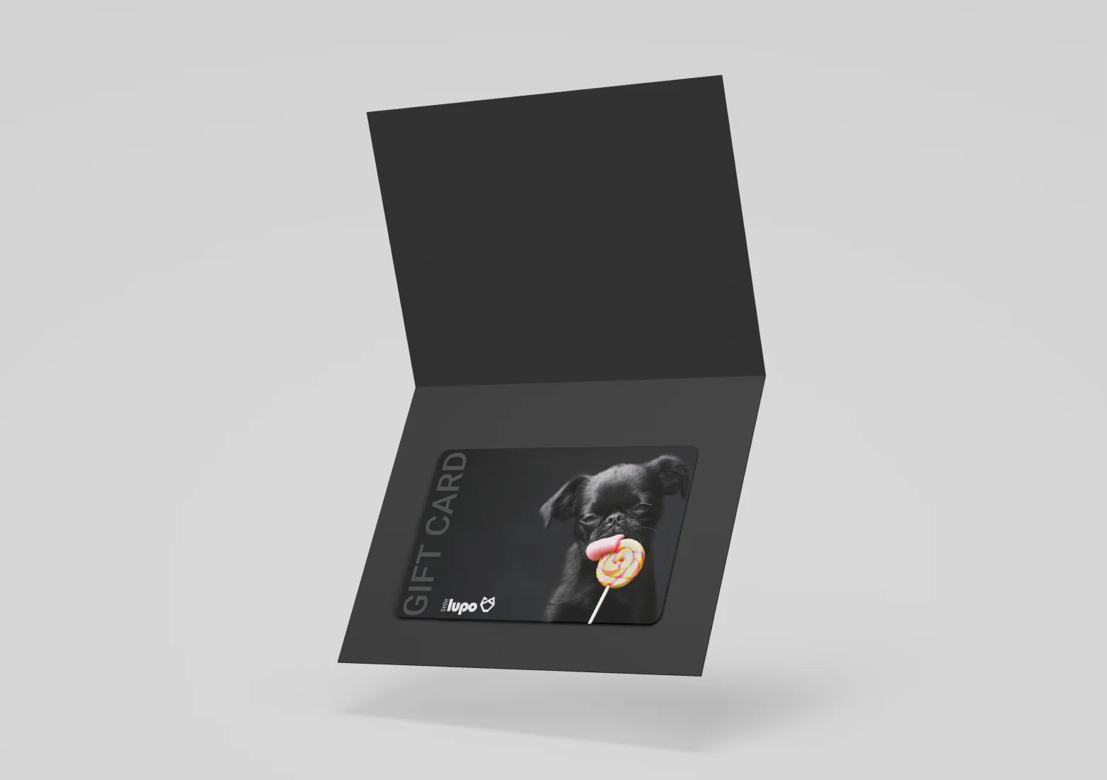 Little Lupo e-gift card illustration: a small black dog on the right, playfully licking a colorful lollipop. The background is dark grey, with the white Little Lupo logo and "Gift Card" text positioned on the left.