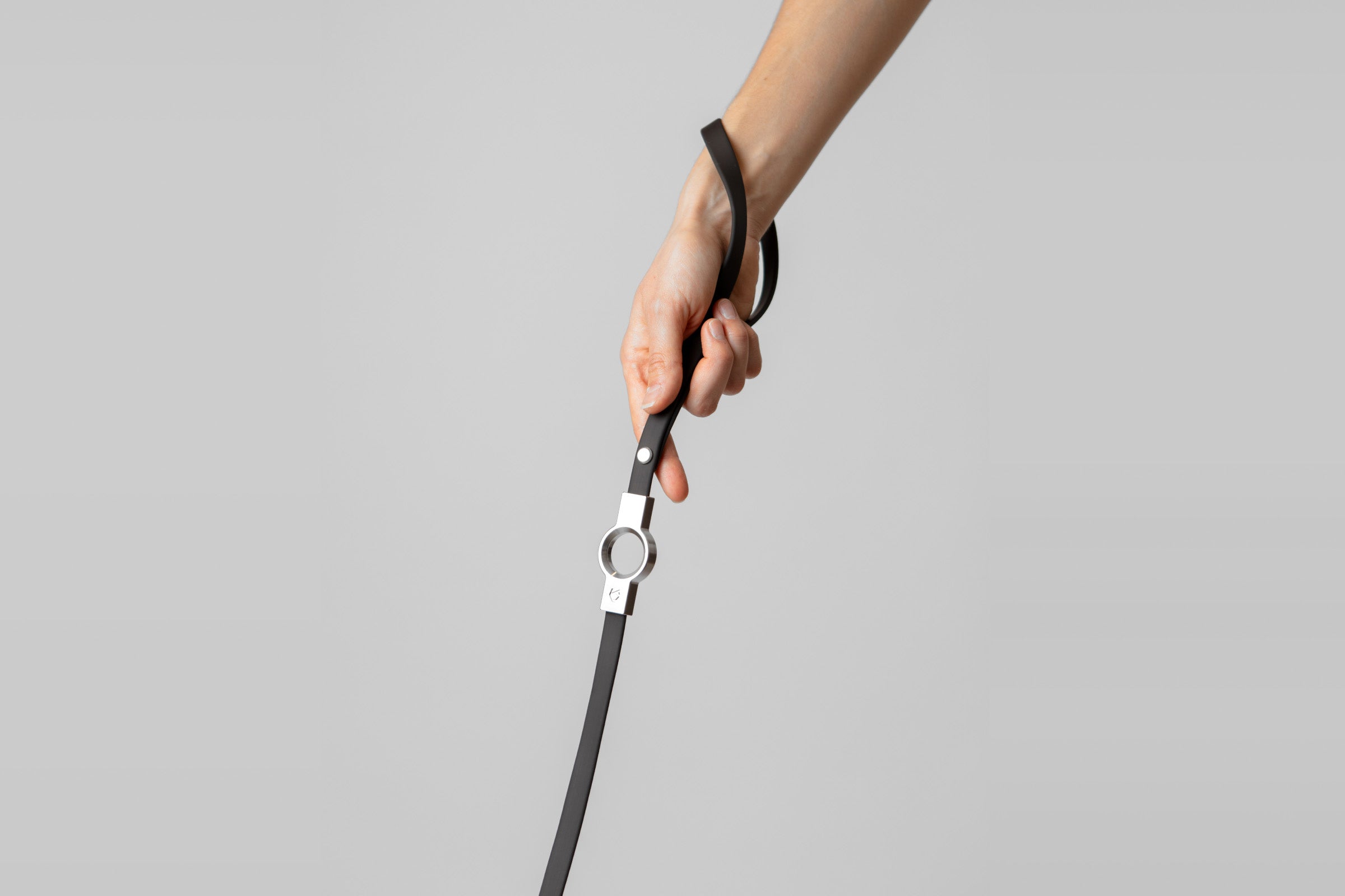 A female hand holding the ergonomic black silicone-coated handle of the Little Lupo Leash L1, emphasizing the comfortable grip and stainless steel connection.