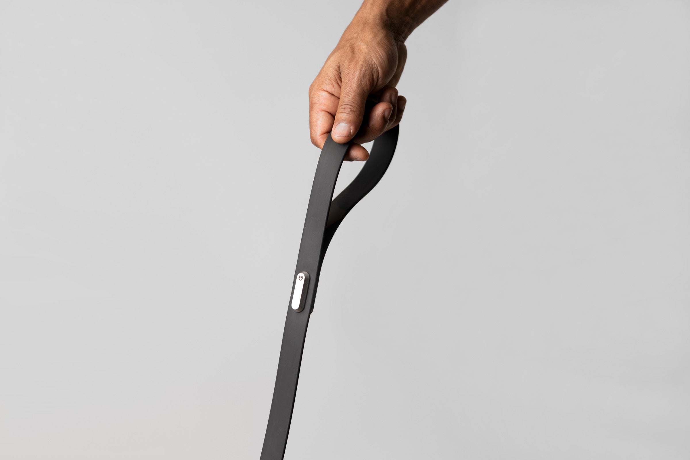 A male hand holding the handle of the Little Lupo Leash L4, demonstrating the comfortable grip of the silicone-coated nylon webbing and the sleek stainless steel connecting monument with the logo engraved.
