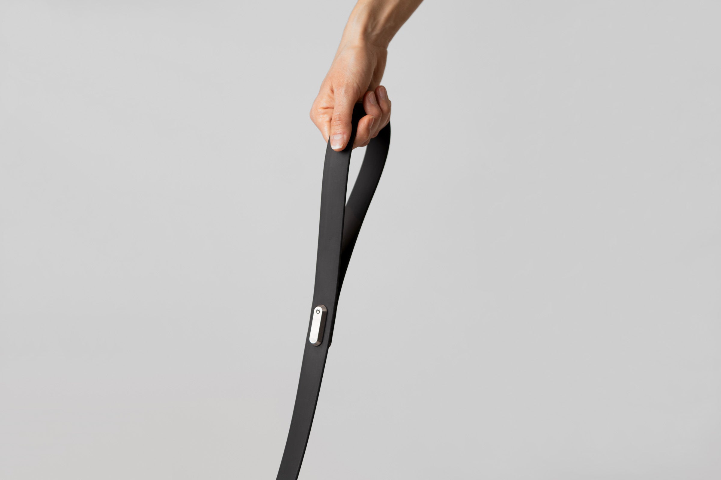 A female hand holding the handle of the Little Lupo Leash L4, demonstrating the comfortable grip of the silicone-coated nylon webbing and the sleek stainless steel connecting monument with the logo engraved.