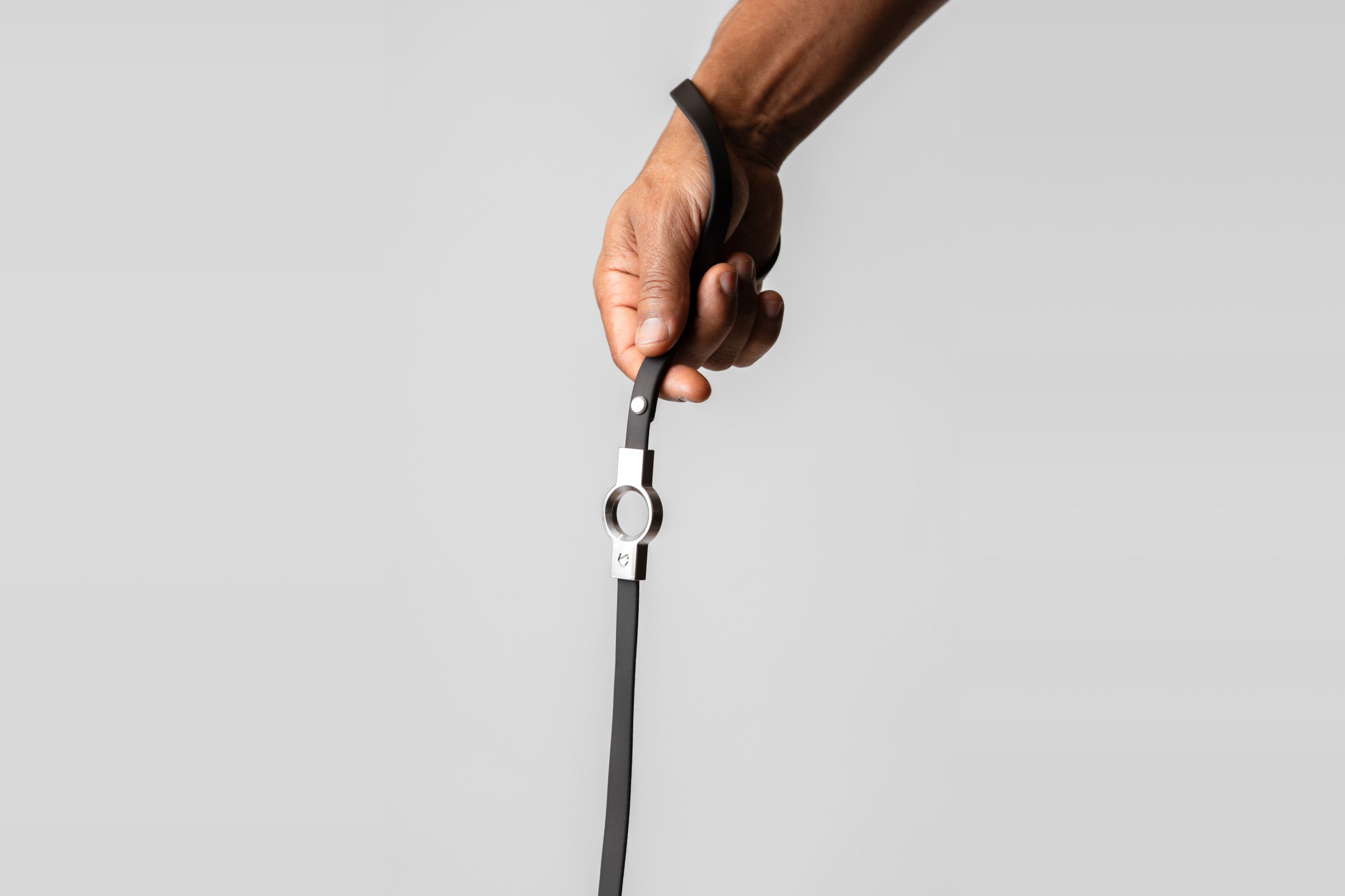 A male hand holding the ergonomic black silicone-coated handle of the Little Lupo Leash L1, emphasizing the comfortable grip and stainless steel connection.
