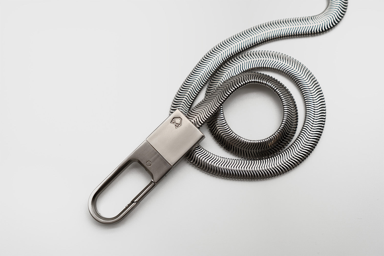 Little Lupo Subtle Strength Leash coiled on a white surface, showcasing the flexible stainless steel chain and the solid clip with the brand logo. 