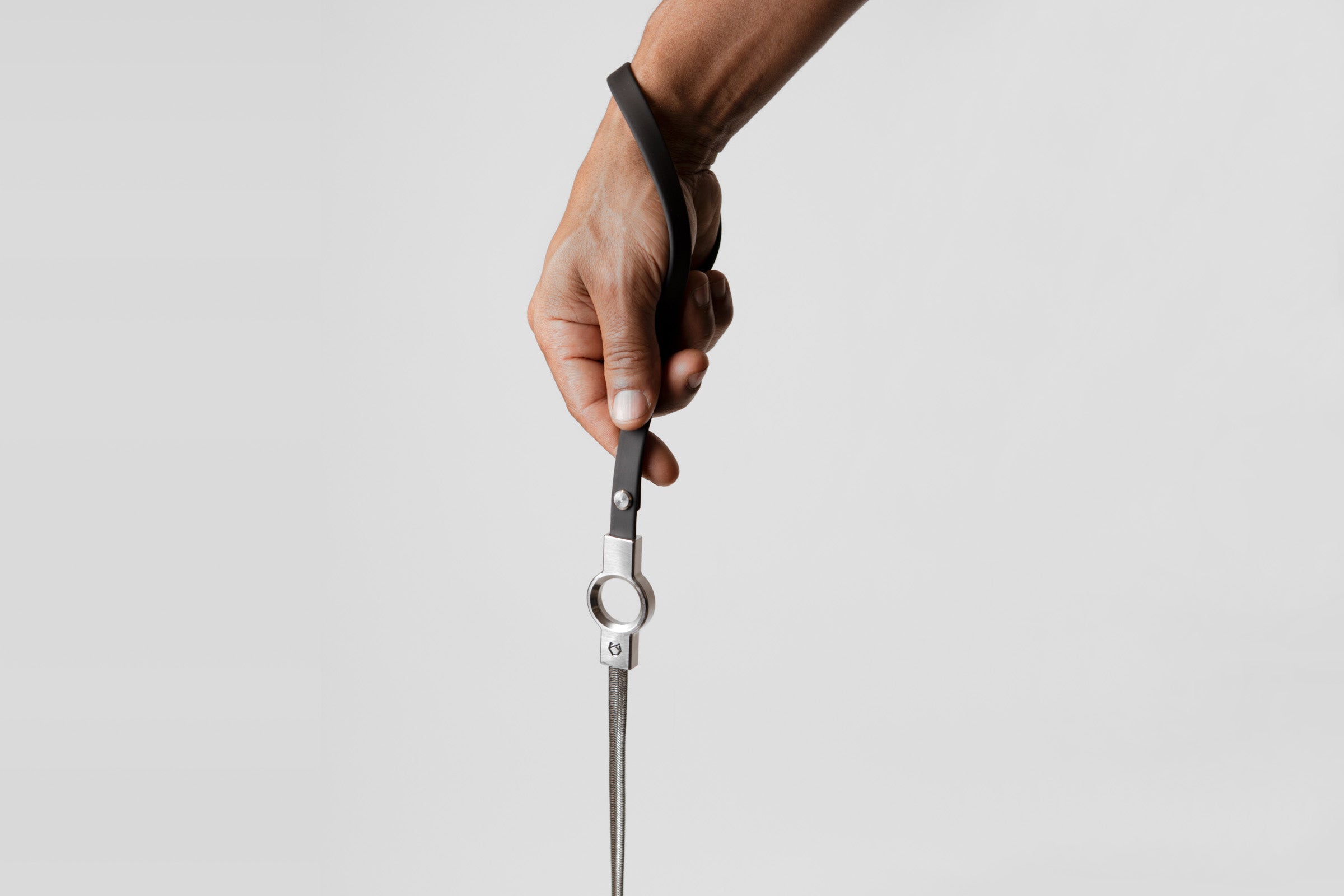 A male hand holding the black silicone coated handle of the Little Lupo Subtle Strength Leash, demonstrating its comfortable grip and the connection to the stainless steel chain. 
