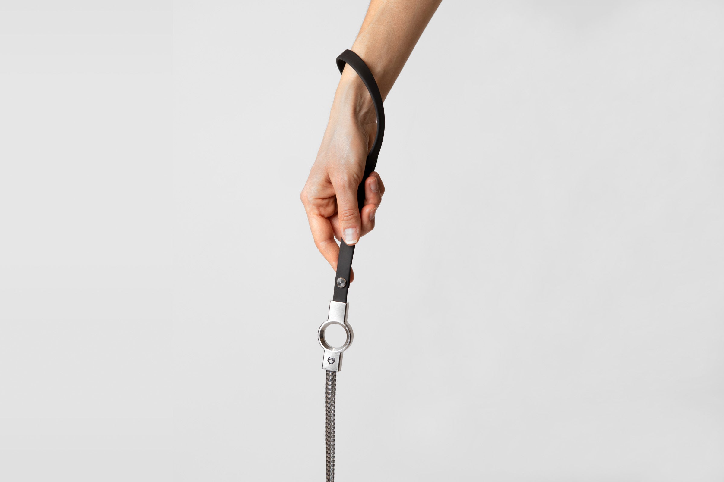 A female hand holding the black silicone coated handle of the Little Lupo Subtle Strength Leash, demonstrating its comfortable grip and the connection to the stainless steel chain.  