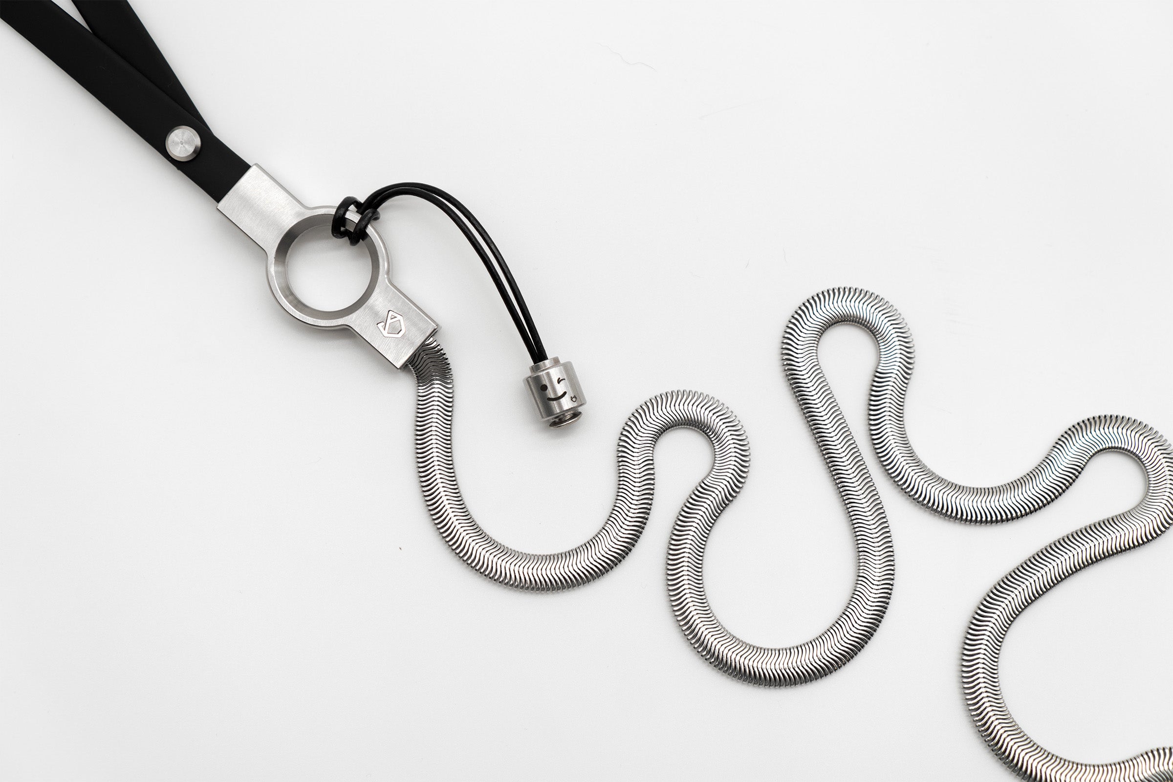 Little Lupo Subtle Strength Leash on white, curled to reveal its flexible stainless steel chain and the characteristic Little Lupo leash pendant with an expressive face.