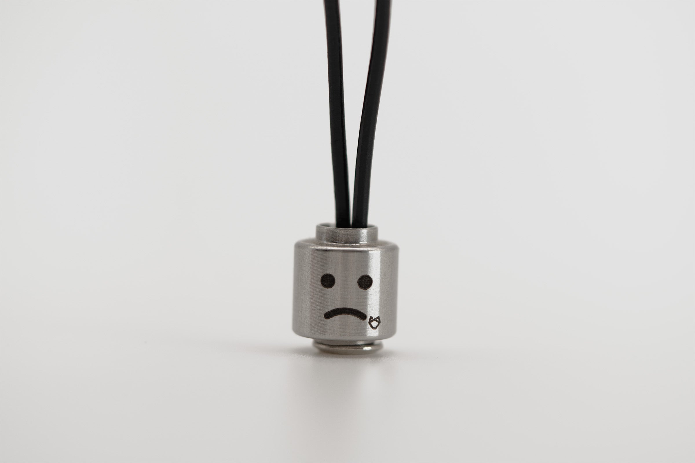 Little Lupo Stainless Steel Pendant featuring a leather black cord and a sad face expression, showcasing the durable metal and detailed etching, designed to add character to dog leashes.